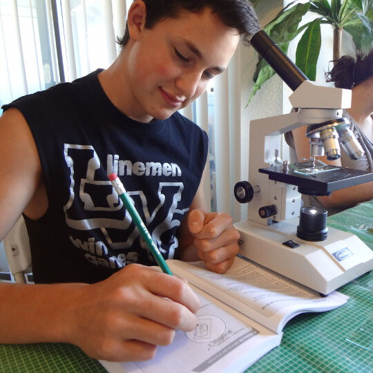 Student studying with microscope and book.